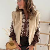 Braune Musselinbluse mit verspielten Blumenstickereien in beige vorne und auf den Armen. Die Bluse hat einen V Ausschnitt mit stehendem Rücschenkragen.