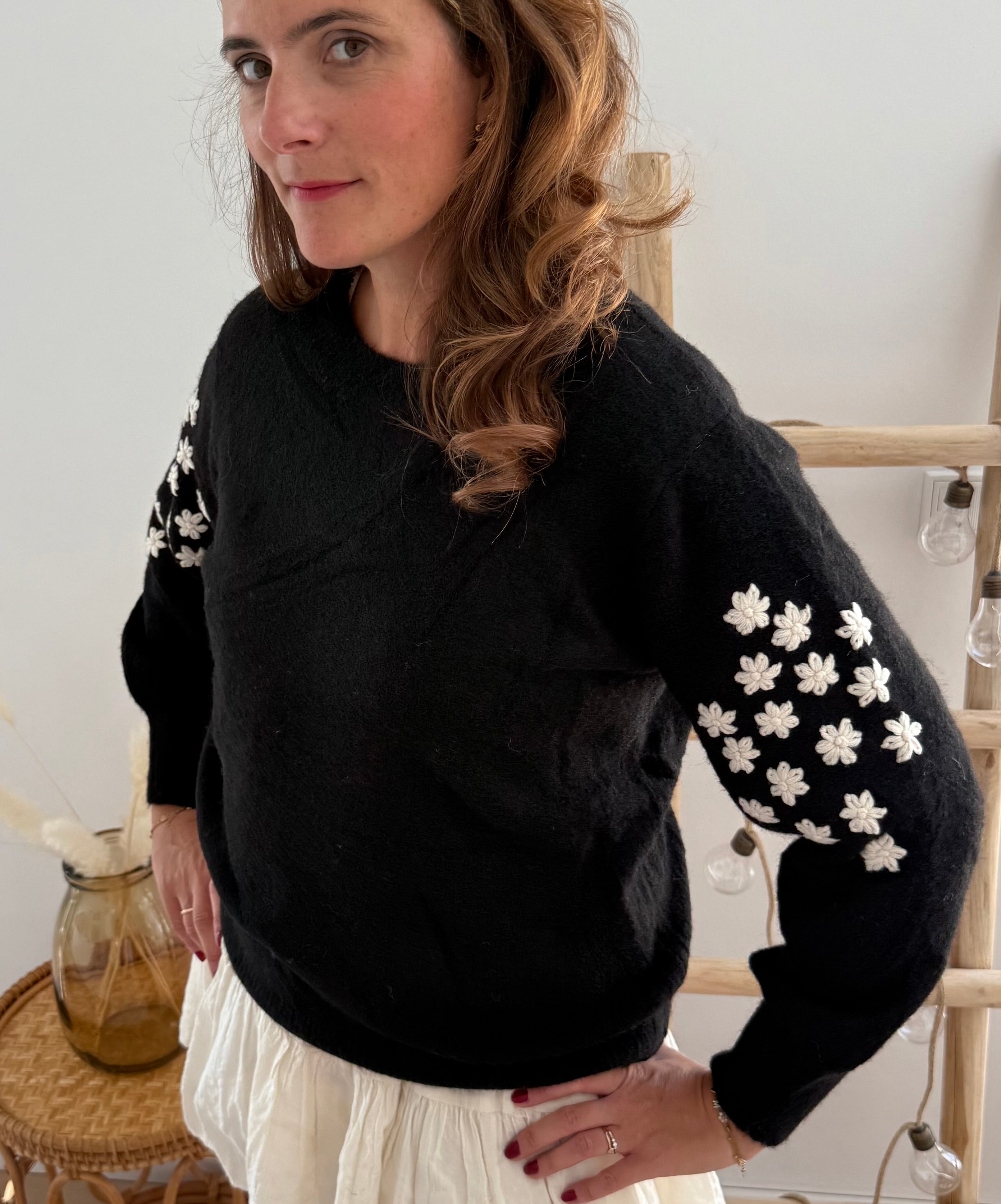 Schwarzer Strickpullover mit verspielten Blumenstickereien auf den Ärmeln in hellbeige.