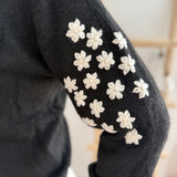 Schwarzer Strickpullover mit verspielten Blumenstickereien auf den Ärmeln in hellbeige.