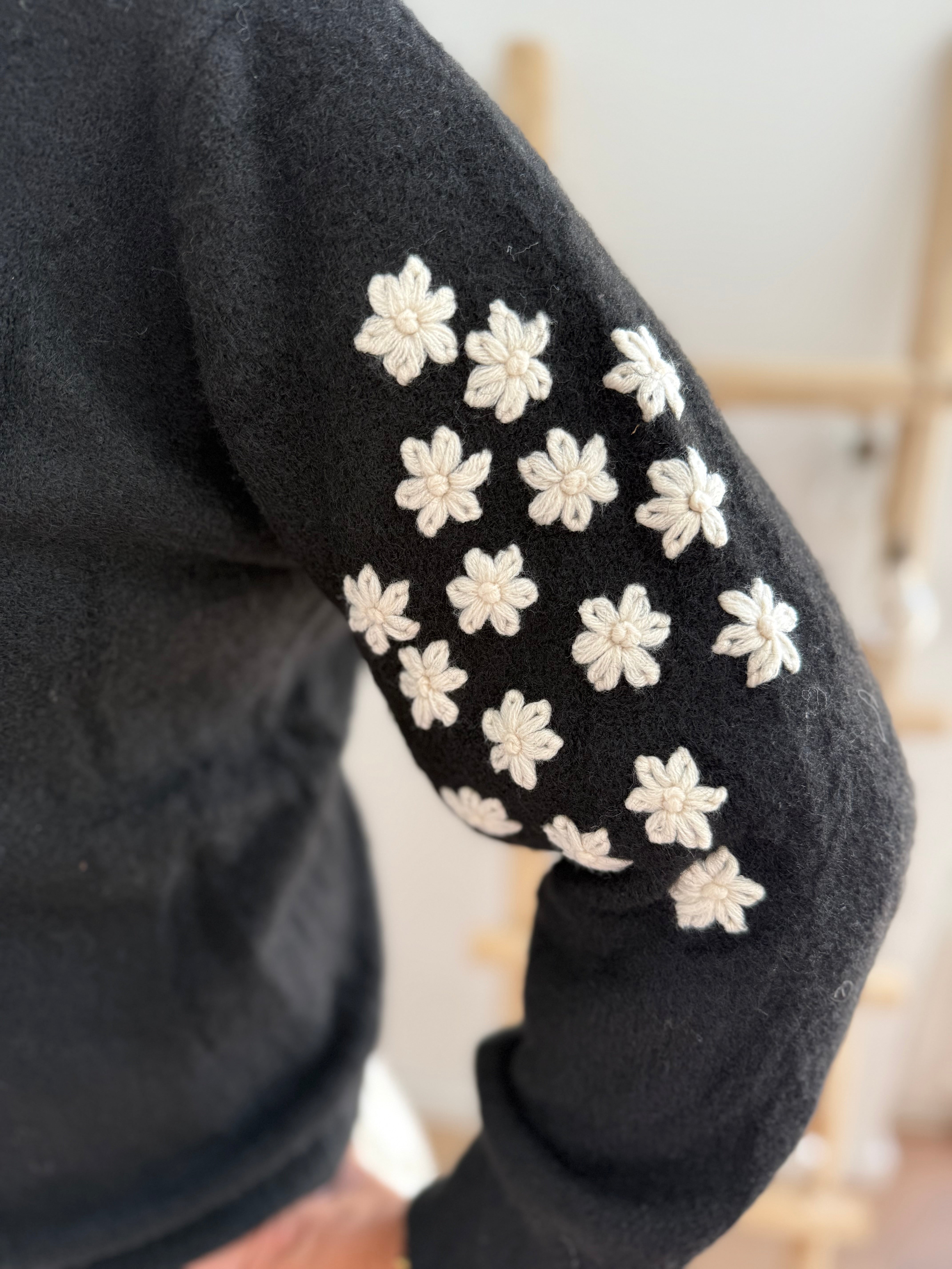 Schwarzer Strickpullover mit verspielten Blumenstickereien auf den Ärmeln in hellbeige.
