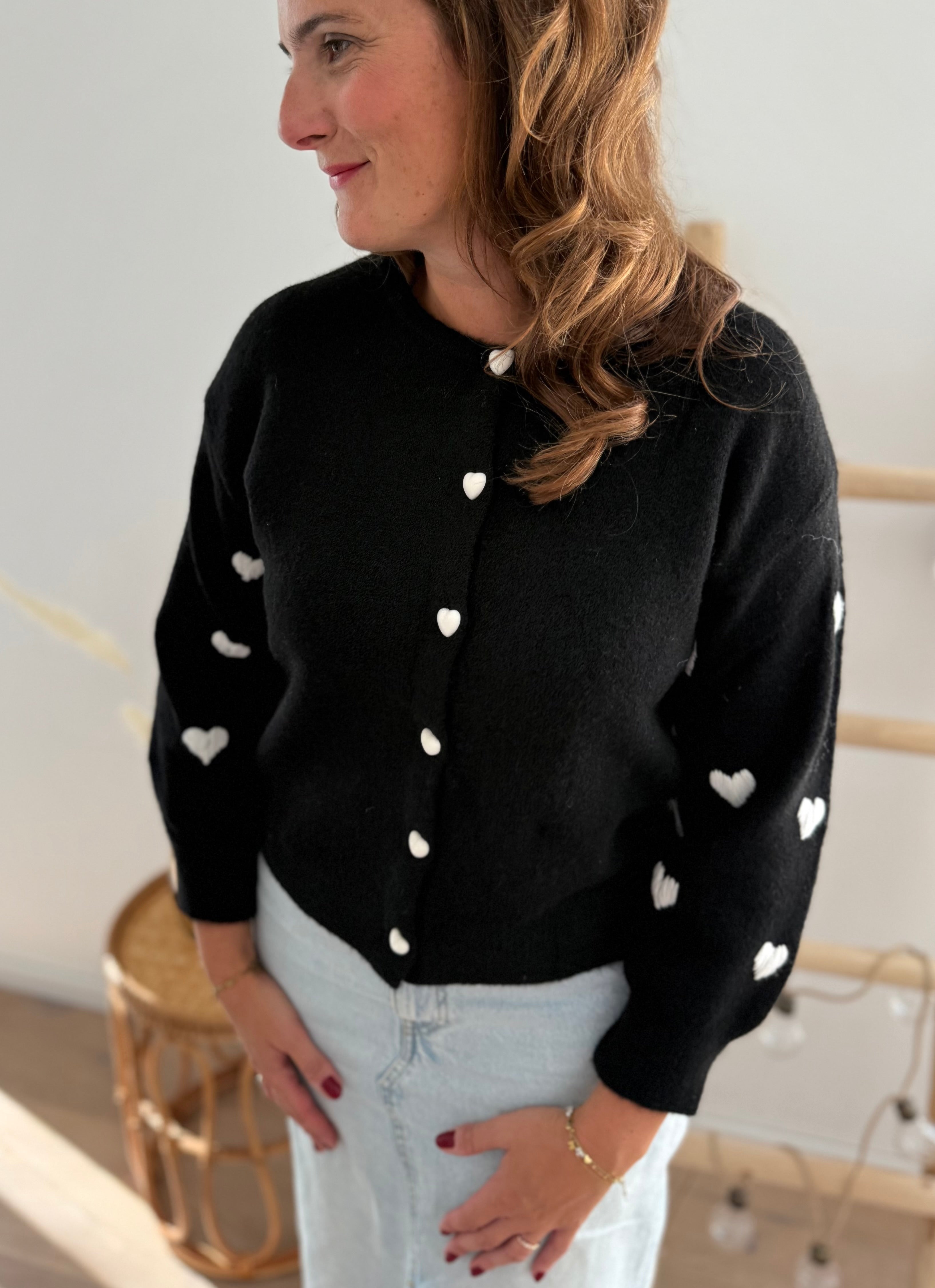 Strickjacke in schwarz mit weißen bestickten Herzen auf den Armen. Die Strickjacke hat einen Rundhalsausschnitt und eine Knopfleiste aus weißen Herzknöpfen.