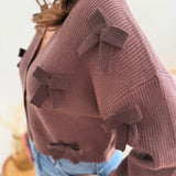Braune Strickjacke mit V Aussschnitt und einem kurzen Cropped Schnitt. Die Strickjacke ist mit braunen Strickschleifen bestickt.