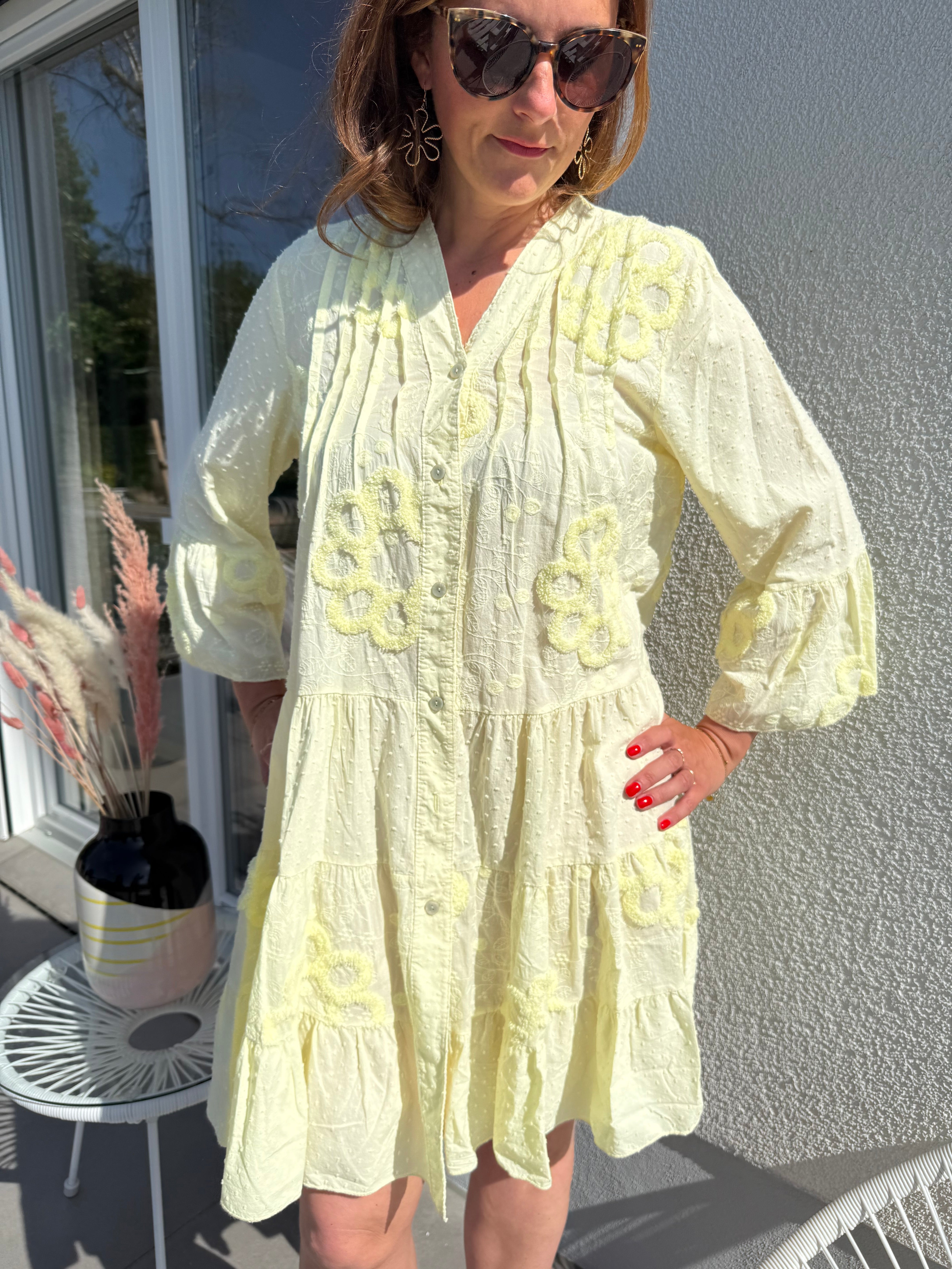 Luftiges kurzes Sommerkleid mit verspielter Blumen Beflockung. Das Kleid fällt locker leicht. Das Kleid hat eine Knopfleiste und einen V Ausschnitt. Die Ärmel sind 3/4 lang. Farbe hellgelb.