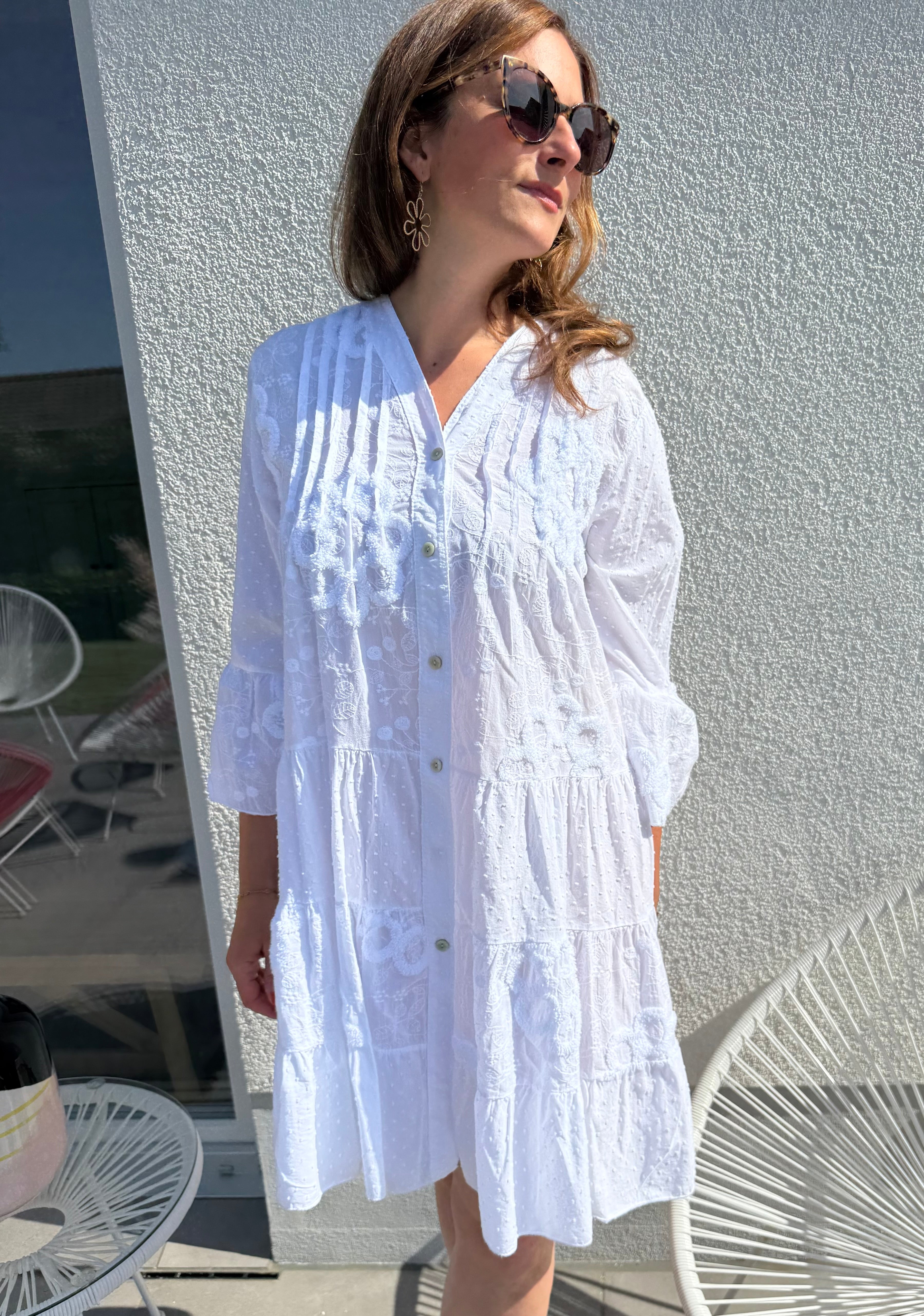Luftiges kurzes Sommerkleid mit verspielter Blumen Beflockung. Das Kleid fällt locker leicht. Das Kleid hat eine Knopfleiste und einen V Ausschnitt. Die Ärmel sind 3/4 lang. Farbe weiß.