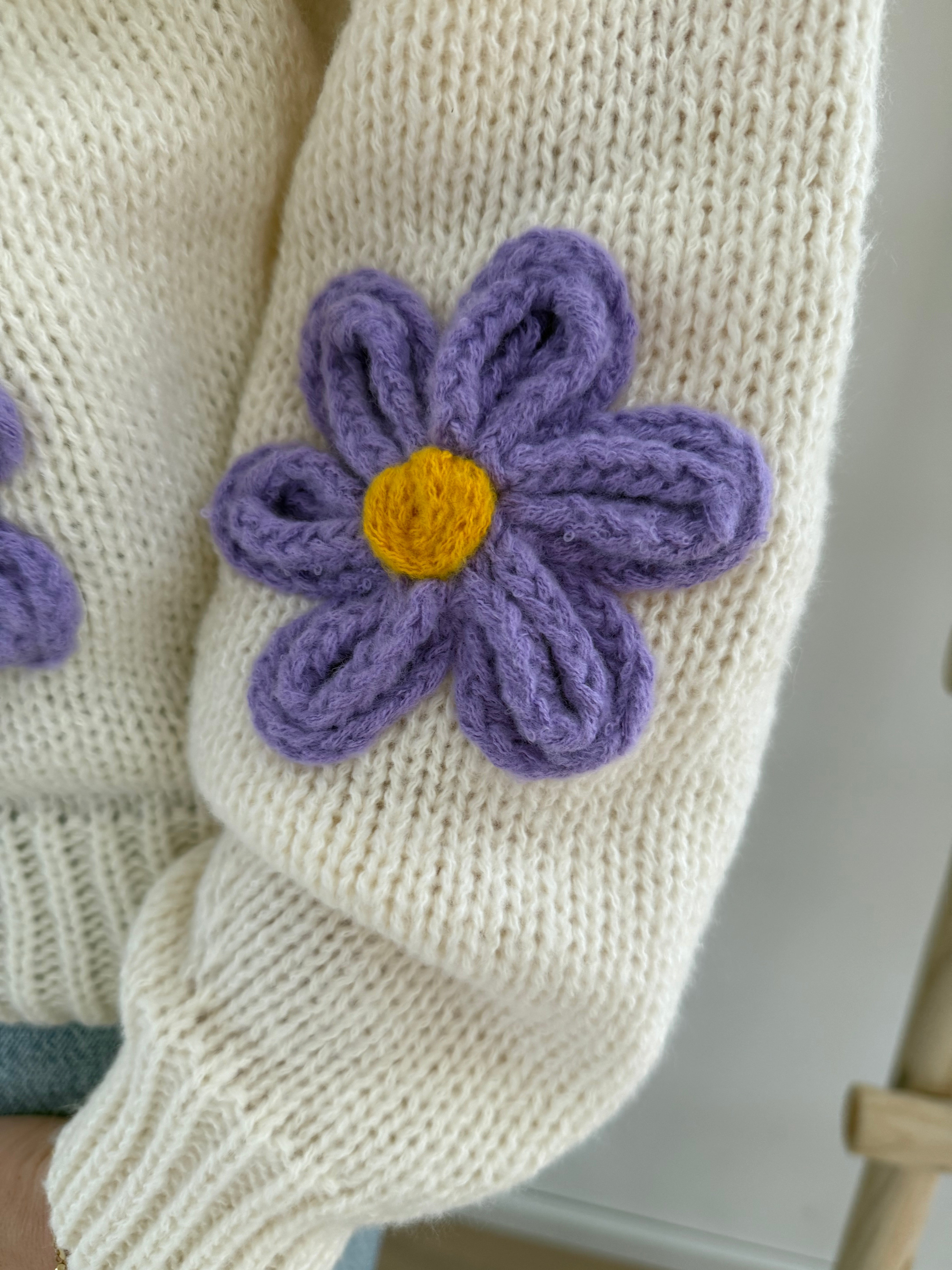 Statement Strickjacke in creme mit wunderschönen großen Blumenapplikationen in gelb und lila in Form einer Margerite . Die Strickjacke fällt locker und hat einen V Ausschnitt.