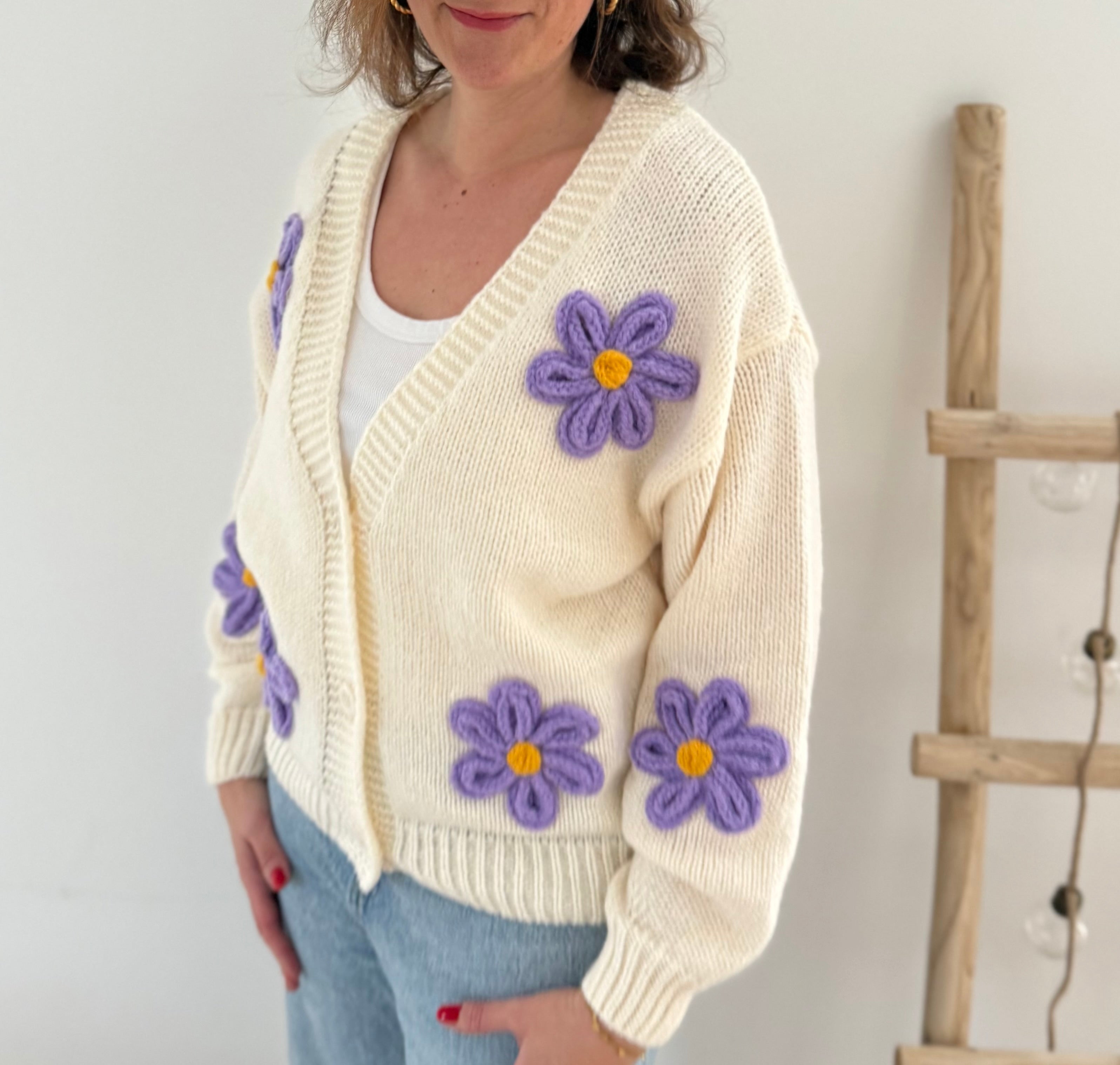 Statement Strickjacke in creme mit wunderschönen großen Blumenapplikationen in gelb und lila in Form einer Margerite . Die Strickjacke fällt locker und hat einen V Ausschnitt.