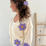 Statement Strickjacke in creme mit wunderschönen großen Blumenapplikationen in gelb und lila in Form einer Margerite . Die Strickjacke fällt locker und hat einen V Ausschnitt.