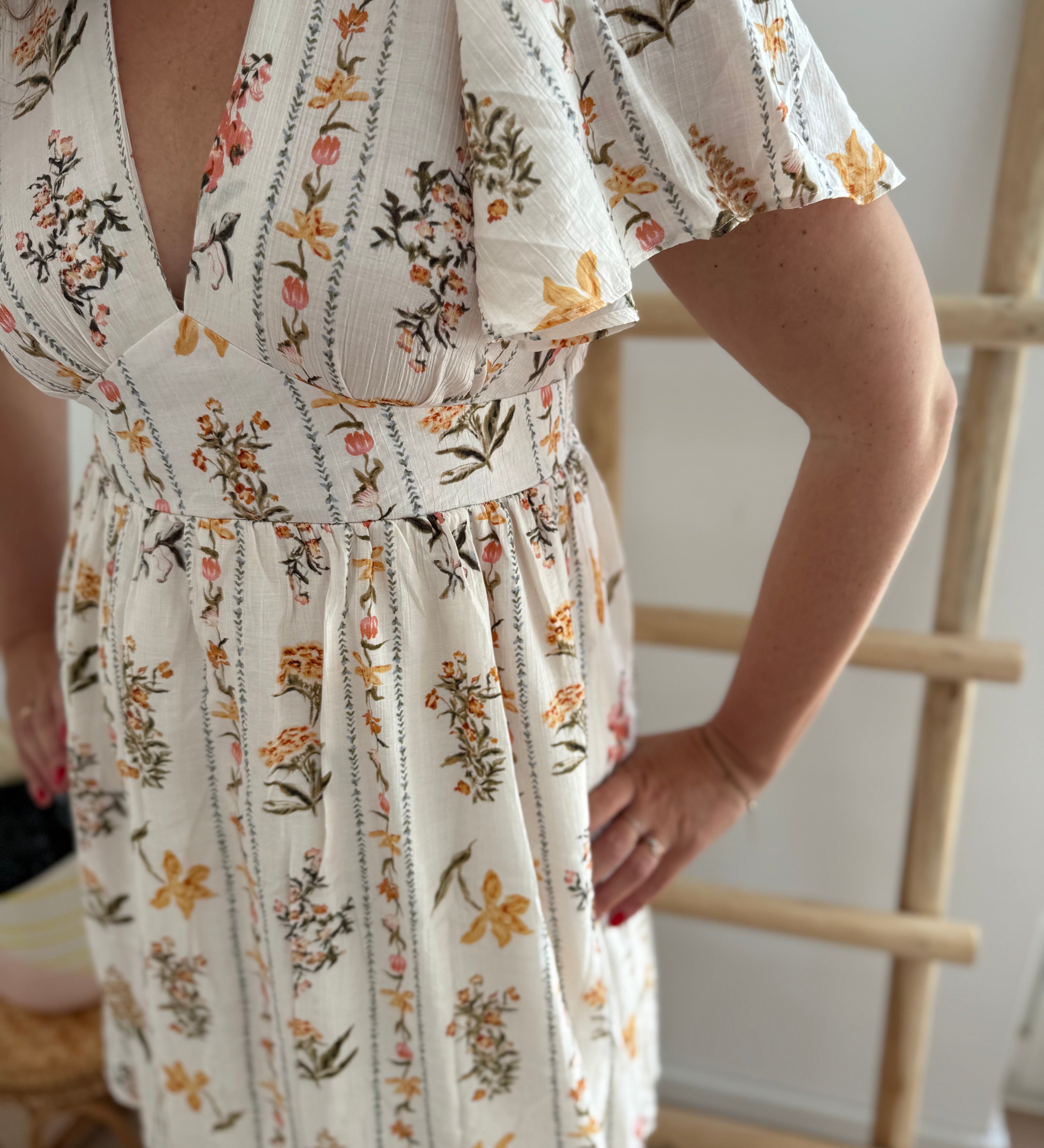 Leichtes kurzes Kleid mit V Ausschnitt und kurzen Flügelärmeln. Das Kleid ist cremefarben mit einem verspielten Blumenmuster in gelb, grün und rot.