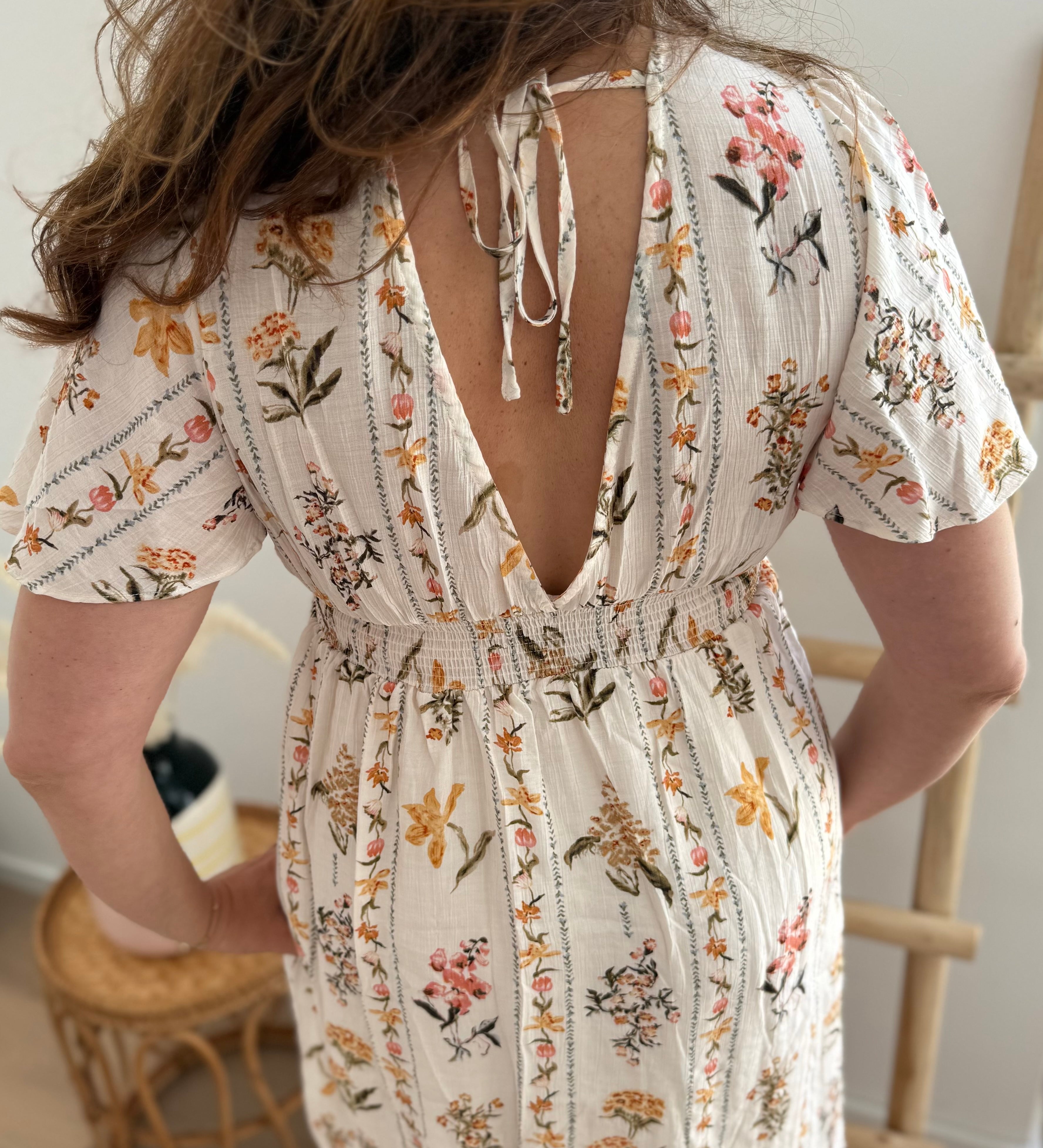Leichtes kurzes Kleid mit V Ausschnitt und kurzen Flügelärmeln. Das Kleid ist cremefarben mit einem verspielten Blumenmuster in gelb, grün und rot.