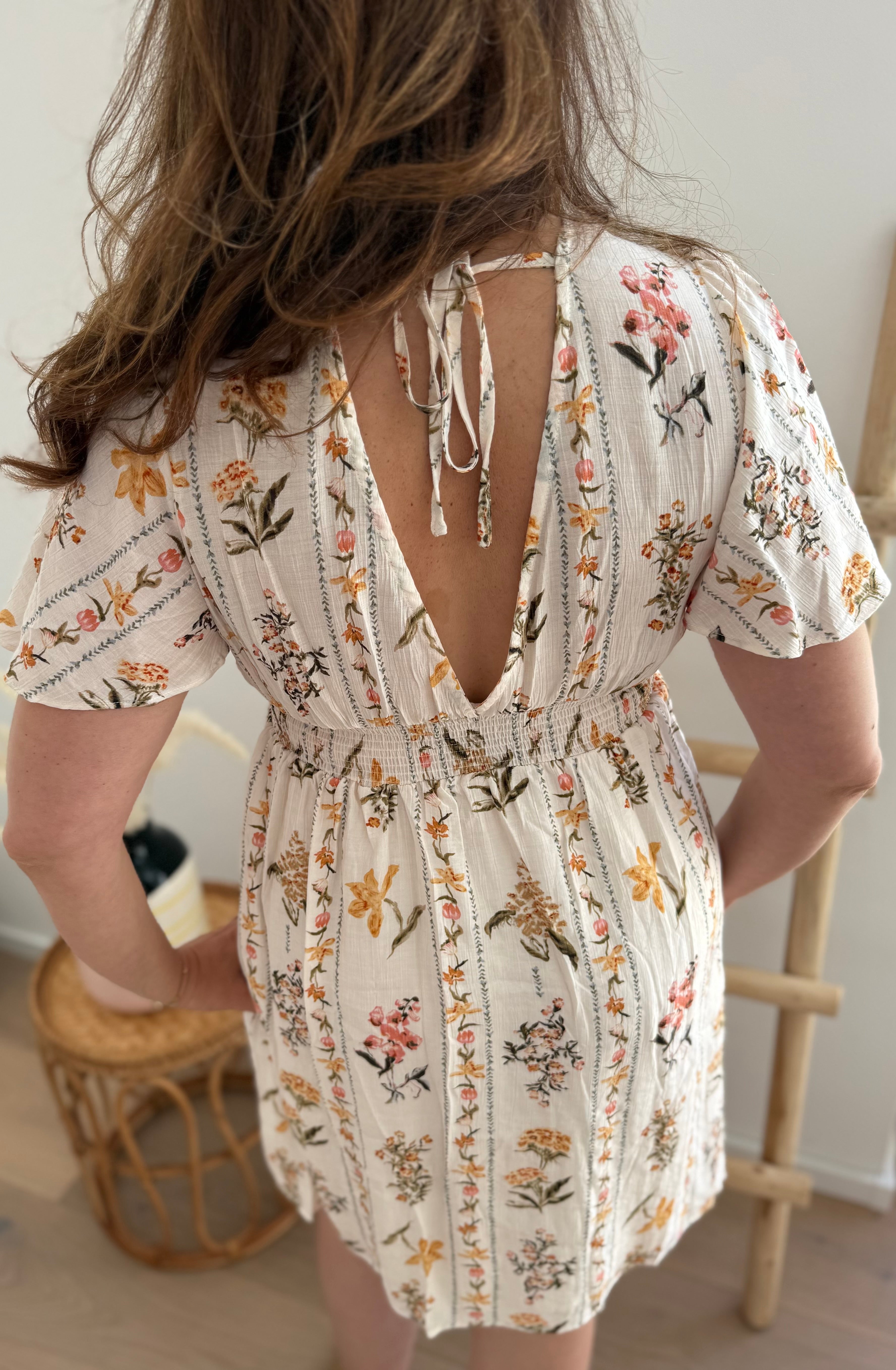 Leichtes kurzes Kleid mit V Ausschnitt und kurzen Flügelärmeln. Das Kleid ist cremefarben mit einem verspielten Blumenmuster in gelb, grün und rot.