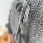 Locker fallende Strickjacke in grau die mit 3 Schleifen vorne zusammen gebunden wird.