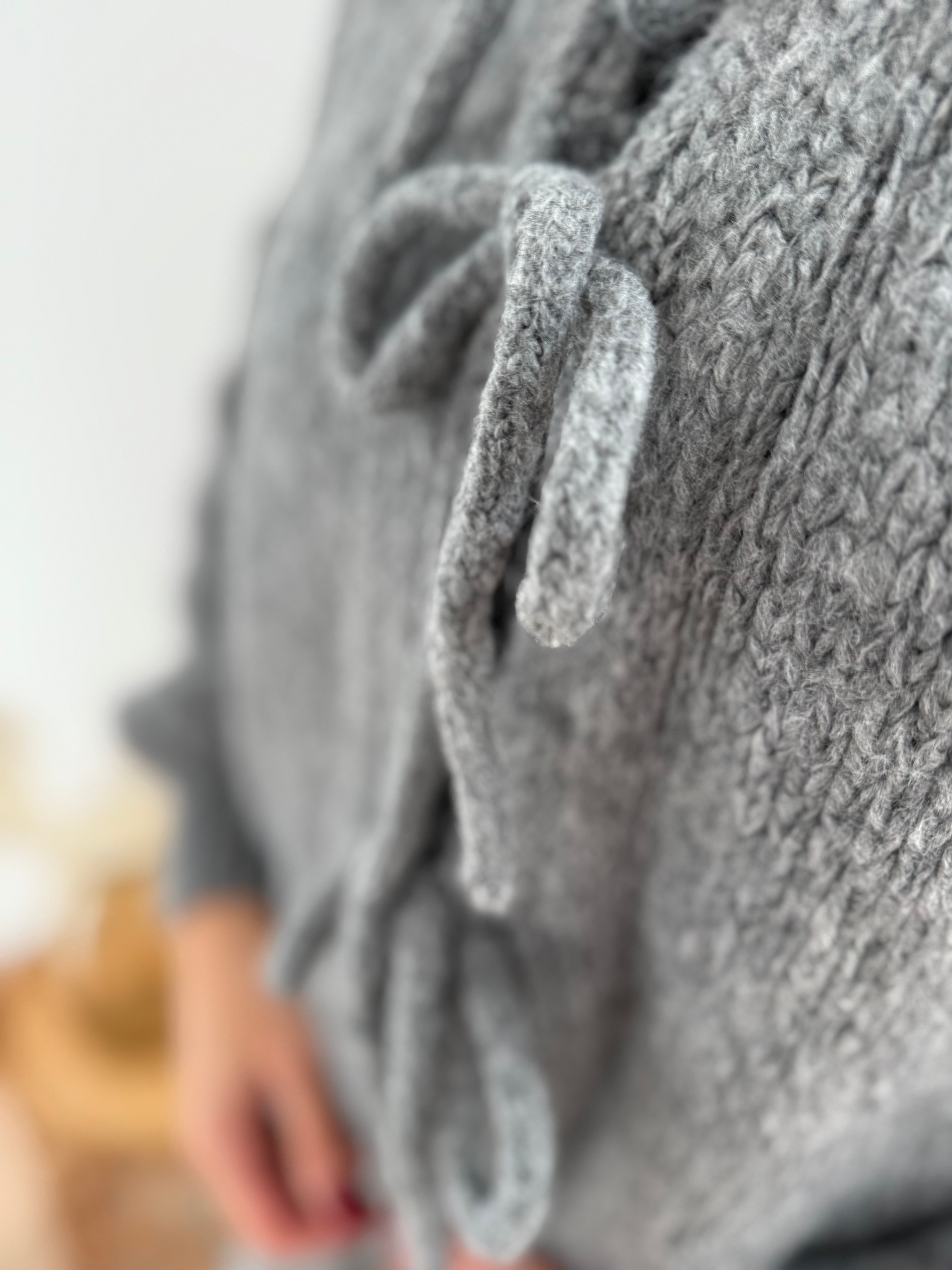 Locker fallende Strickjacke in grau die mit 3 Schleifen vorne zusammen gebunden wird.