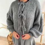 Locker fallende Strickjacke in grau die mit 3 Schleifen vorne zusammen gebunden wird.