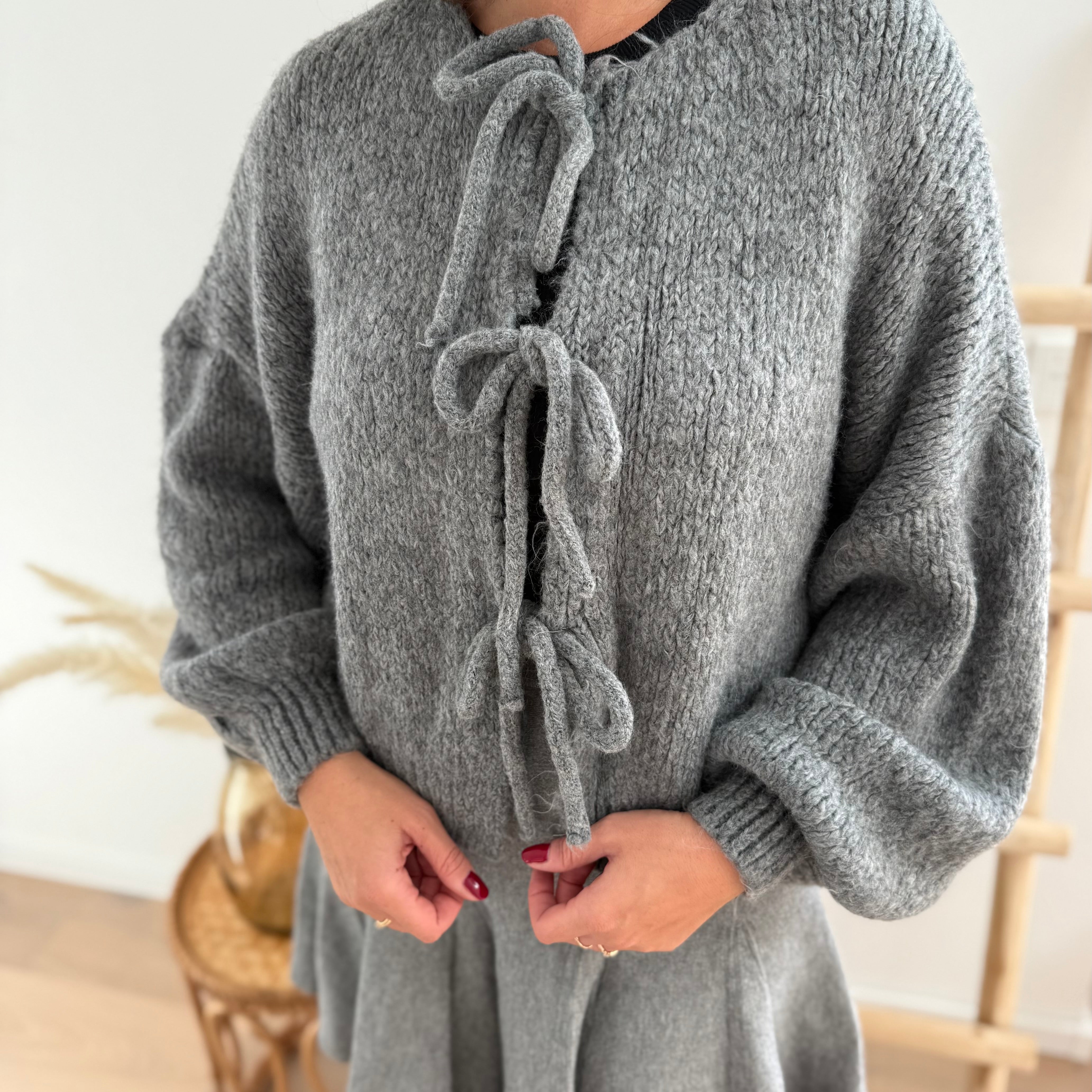 Locker fallende Strickjacke in grau die mit 3 Schleifen vorne zusammen gebunden wird.