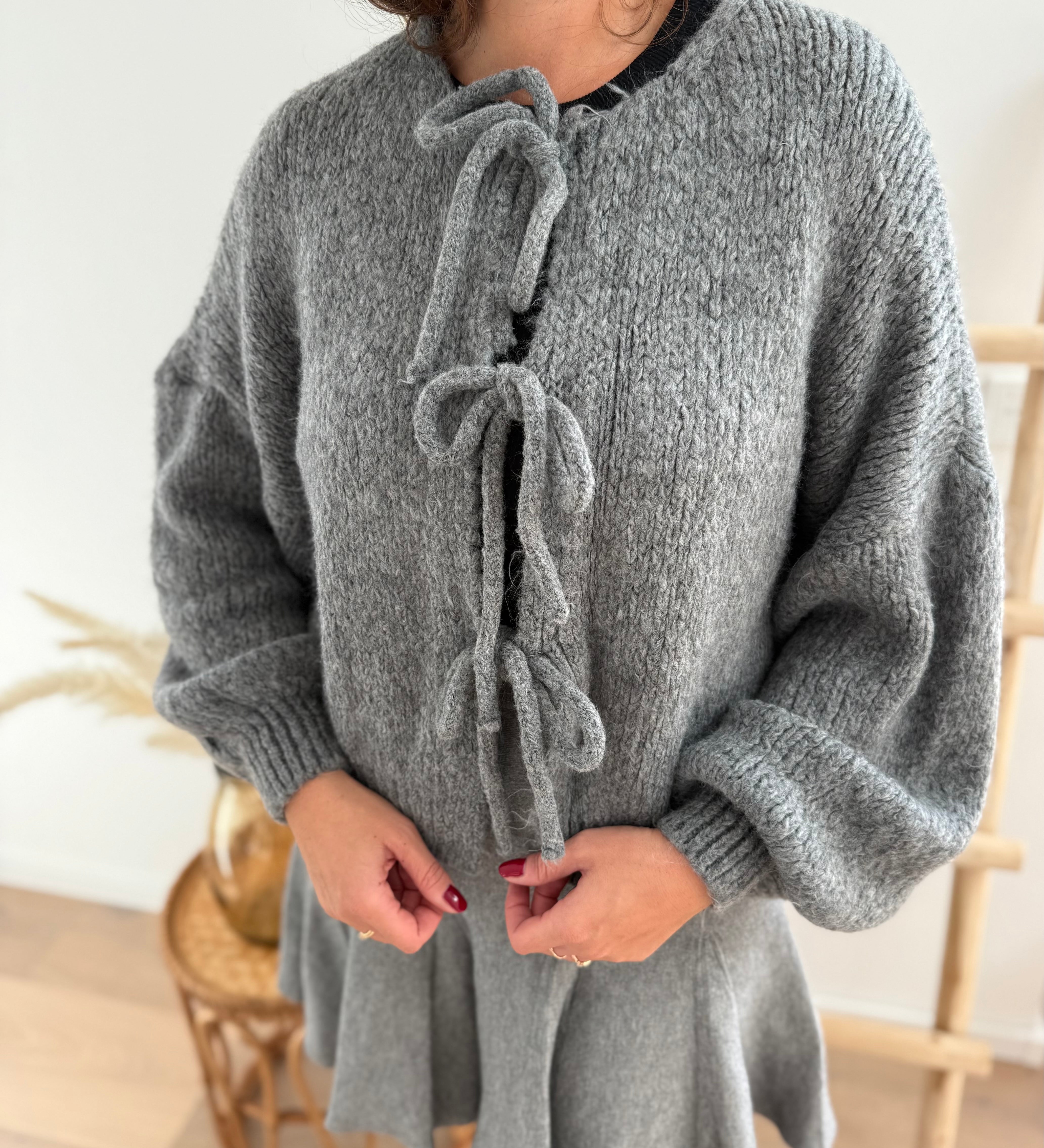 Locker fallende Strickjacke in grau die mit 3 Schleifen vorne zusammen gebunden wird.