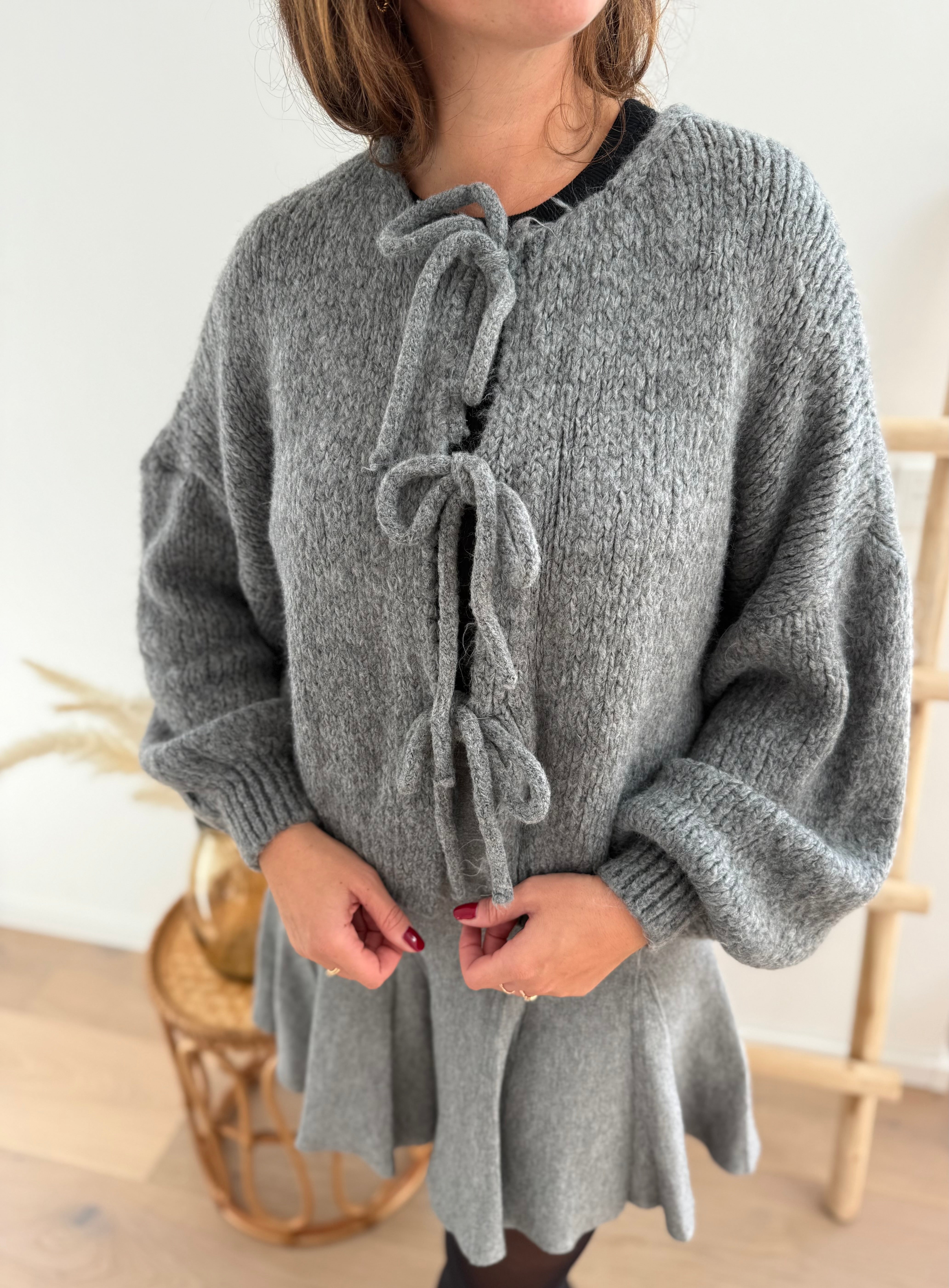 Locker fallende Strickjacke in grau die mit 3 Schleifen vorne zusammen gebunden wird.