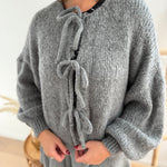 Locker fallende Strickjacke in grau die mit 3 Schleifen vorne zusammen gebunden wird.