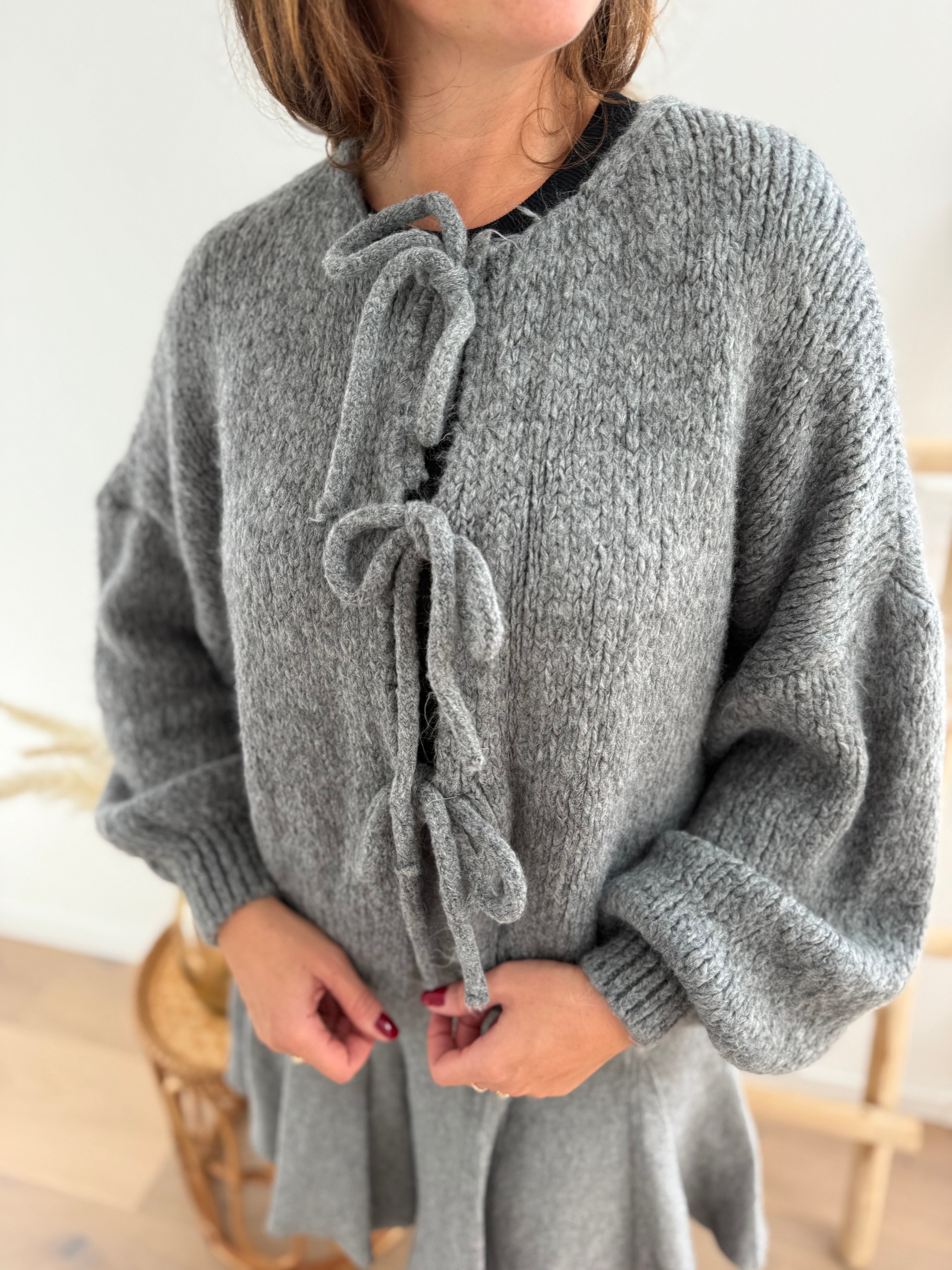 Locker fallende Strickjacke in grau die mit 3 Schleifen vorne zusammen gebunden wird.