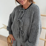 Locker fallende Strickjacke in grau die mit 3 Schleifen vorne zusammen gebunden wird.
