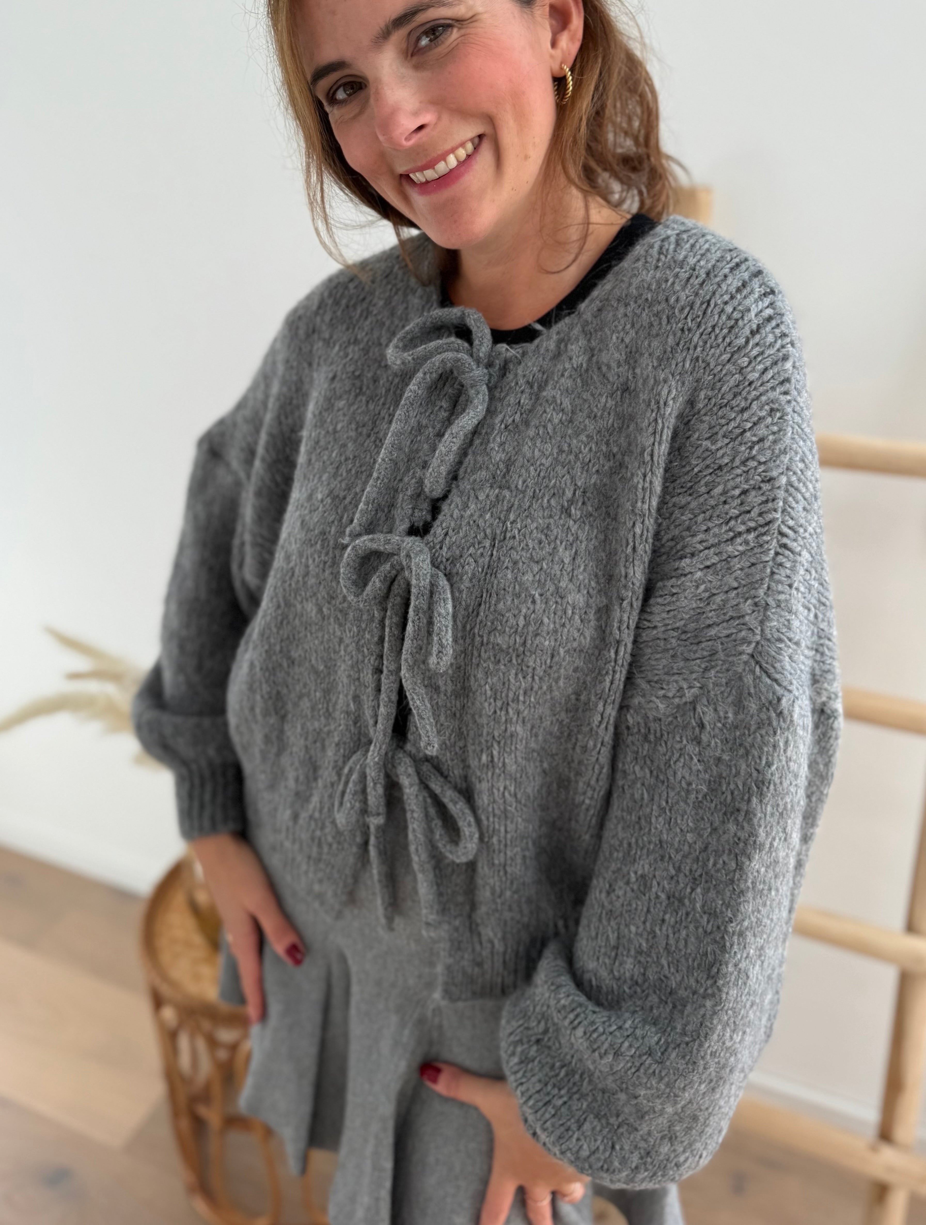 Locker fallende Strickjacke in grau die mit 3 Schleifen vorne zusammen gebunden wird.