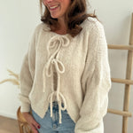 Locker fallende Strickjacke in cremeweiß die mit 3 Schleifen vorne zusammen gebunden wird.