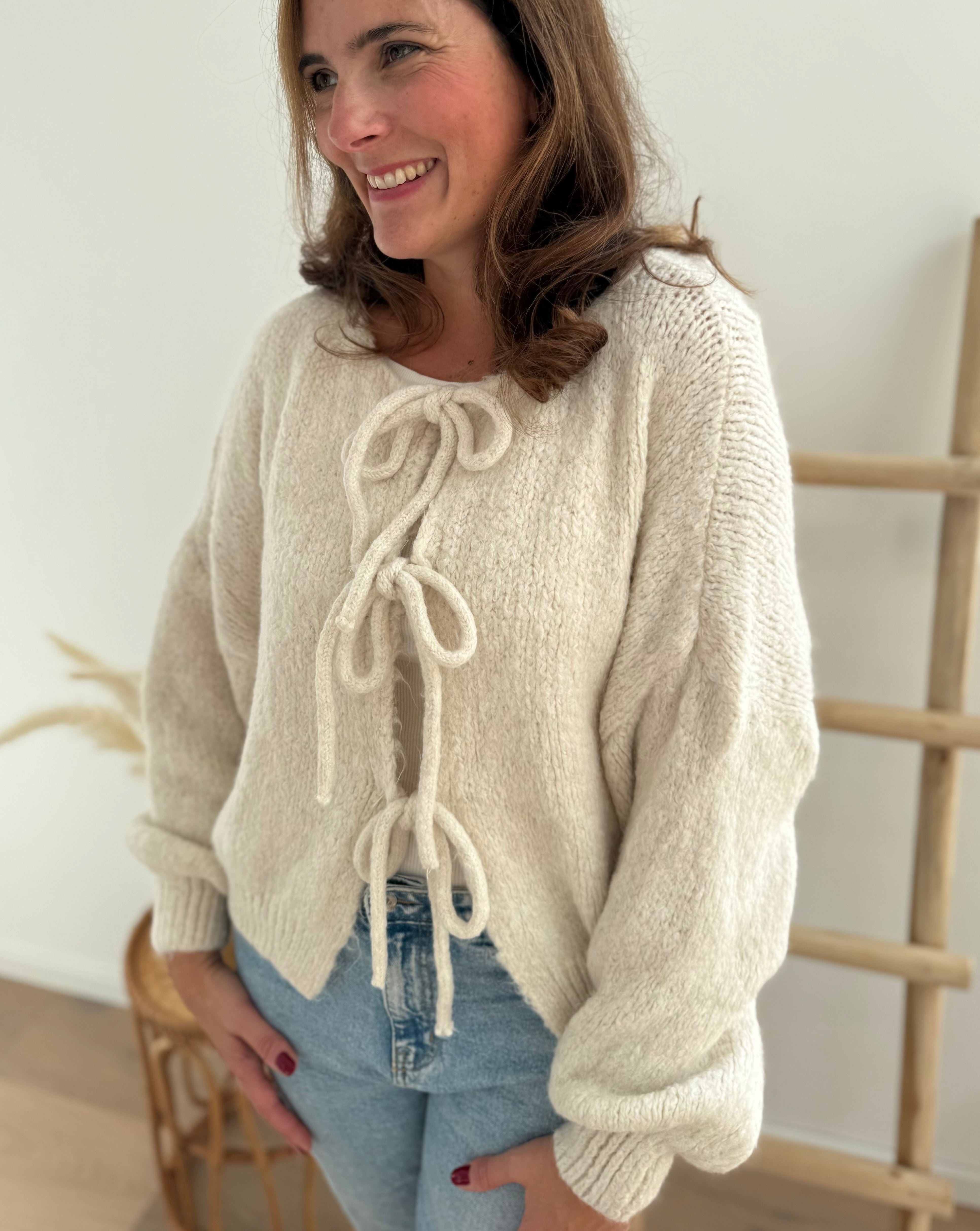 Locker fallende Strickjacke in cremeweiß die mit 3 Schleifen vorne zusammen gebunden wird.