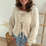 Locker fallende Strickjacke in cremeweiß die mit 3 Schleifen vorne zusammen gebunden wird.