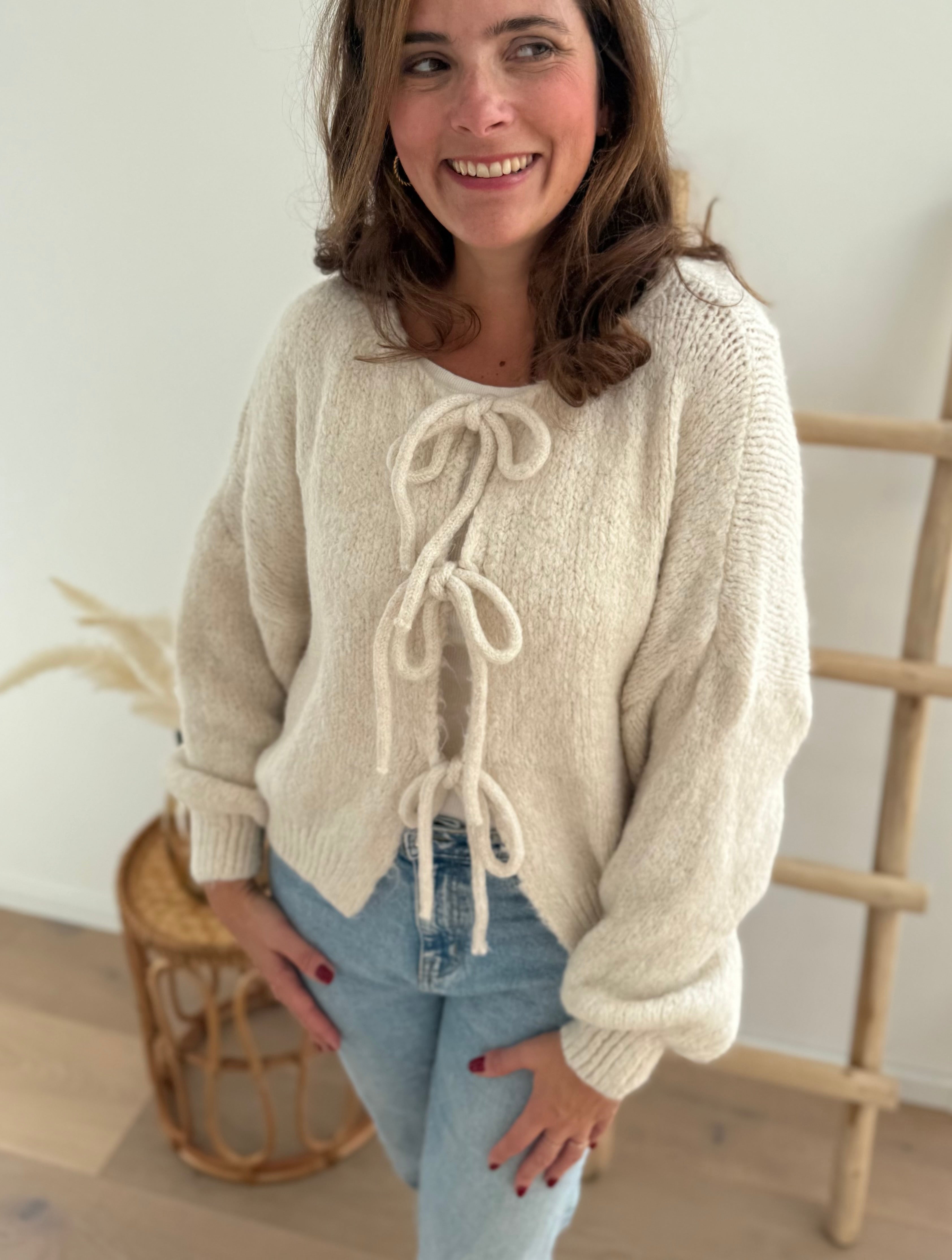 Locker fallende Strickjacke in cremeweiß die mit 3 Schleifen vorne zusammen gebunden wird.