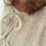 Locker fallende Strickjacke in cremeweiß die mit 3 Schleifen vorne zusammen gebunden wird.