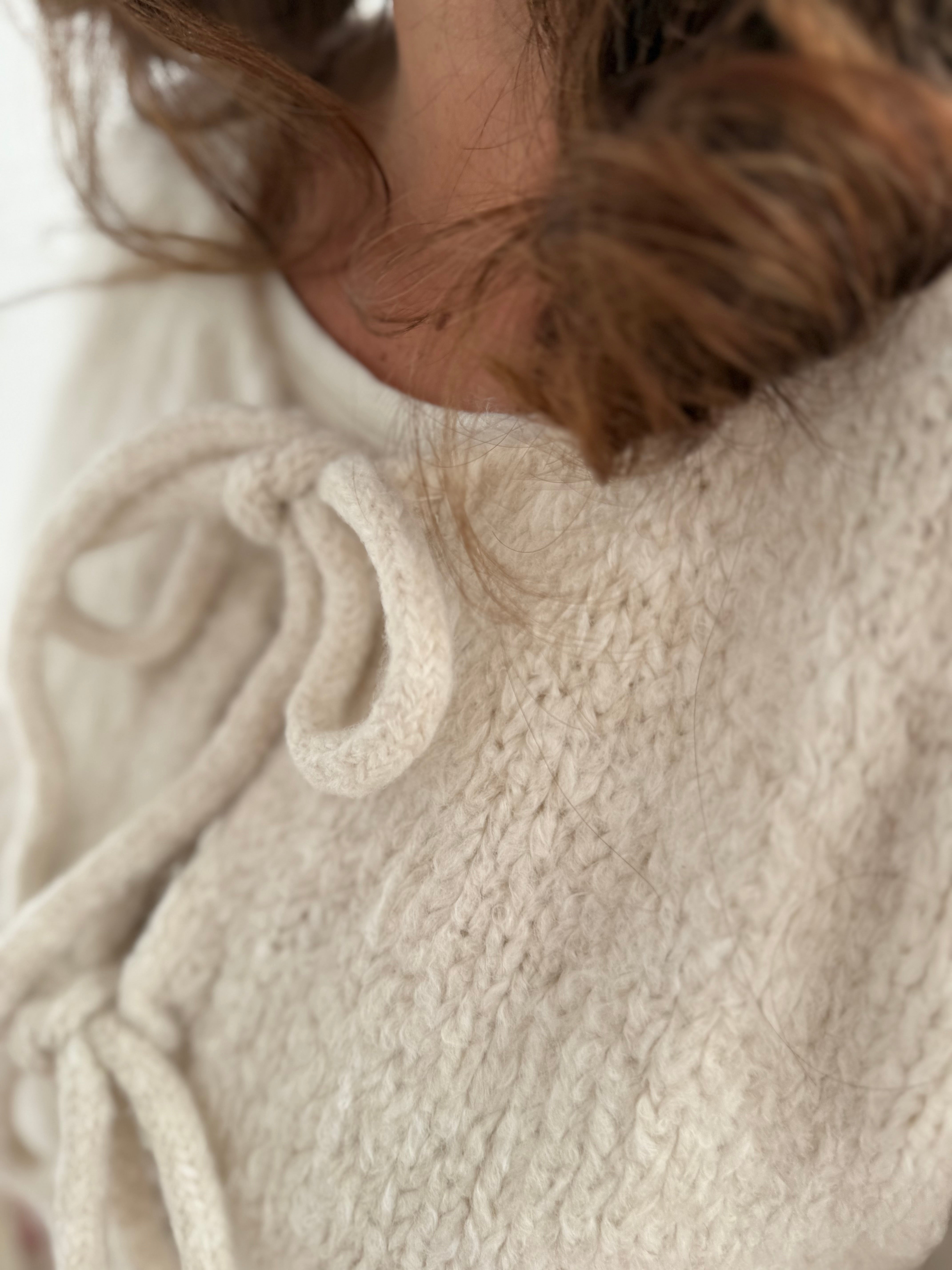 Locker fallende Strickjacke in cremeweiß die mit 3 Schleifen vorne zusammen gebunden wird.