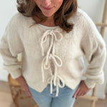 Locker fallende Strickjacke in cremeweiß die mit 3 Schleifen vorne zusammen gebunden wird.