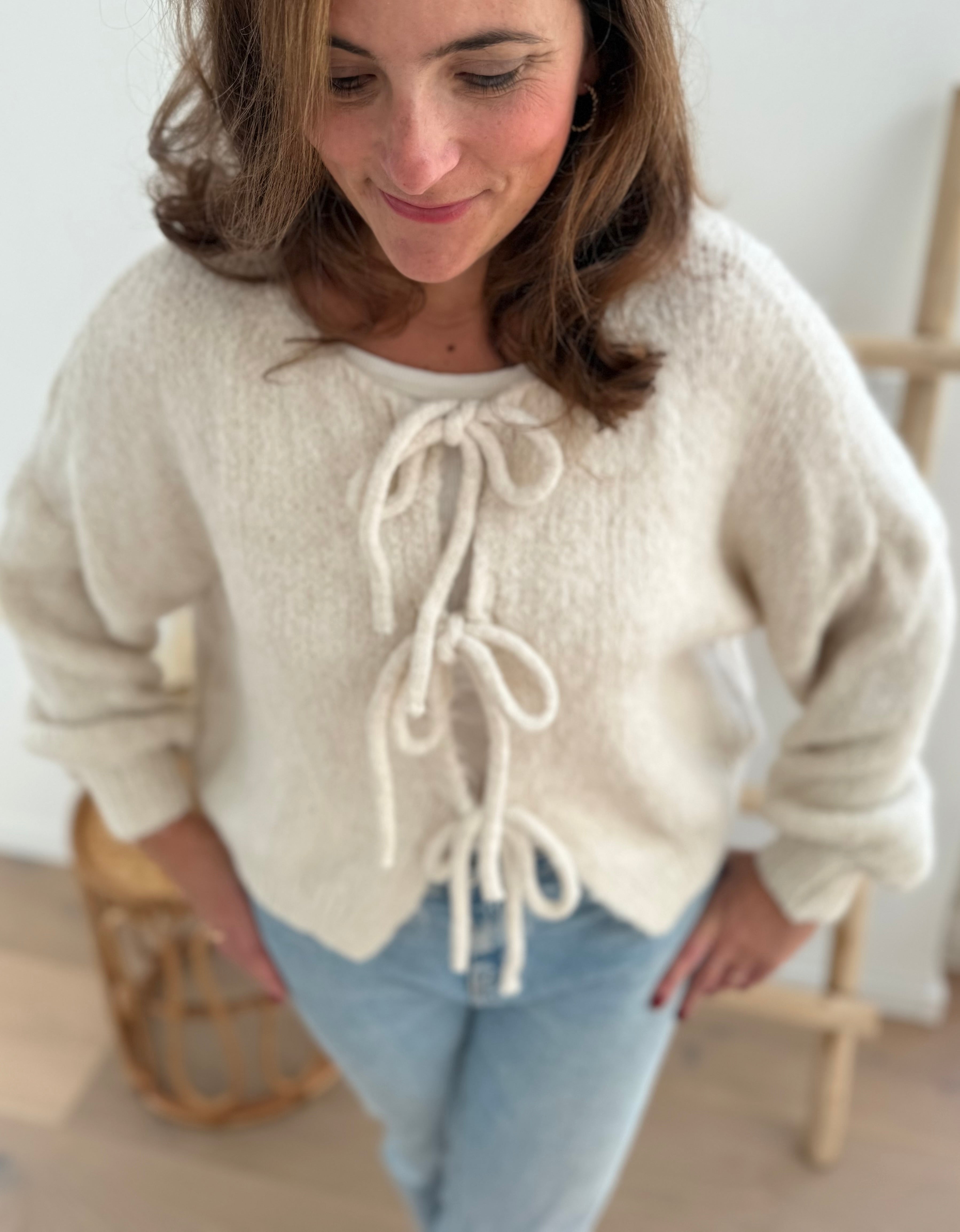 Locker fallende Strickjacke in cremeweiß die mit 3 Schleifen vorne zusammen gebunden wird.