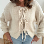 Locker fallende Strickjacke in cremeweiß die mit 3 Schleifen vorne zusammen gebunden wird.