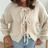 Locker fallende Strickjacke in cremeweiß die mit 3 Schleifen vorne zusammen gebunden wird.