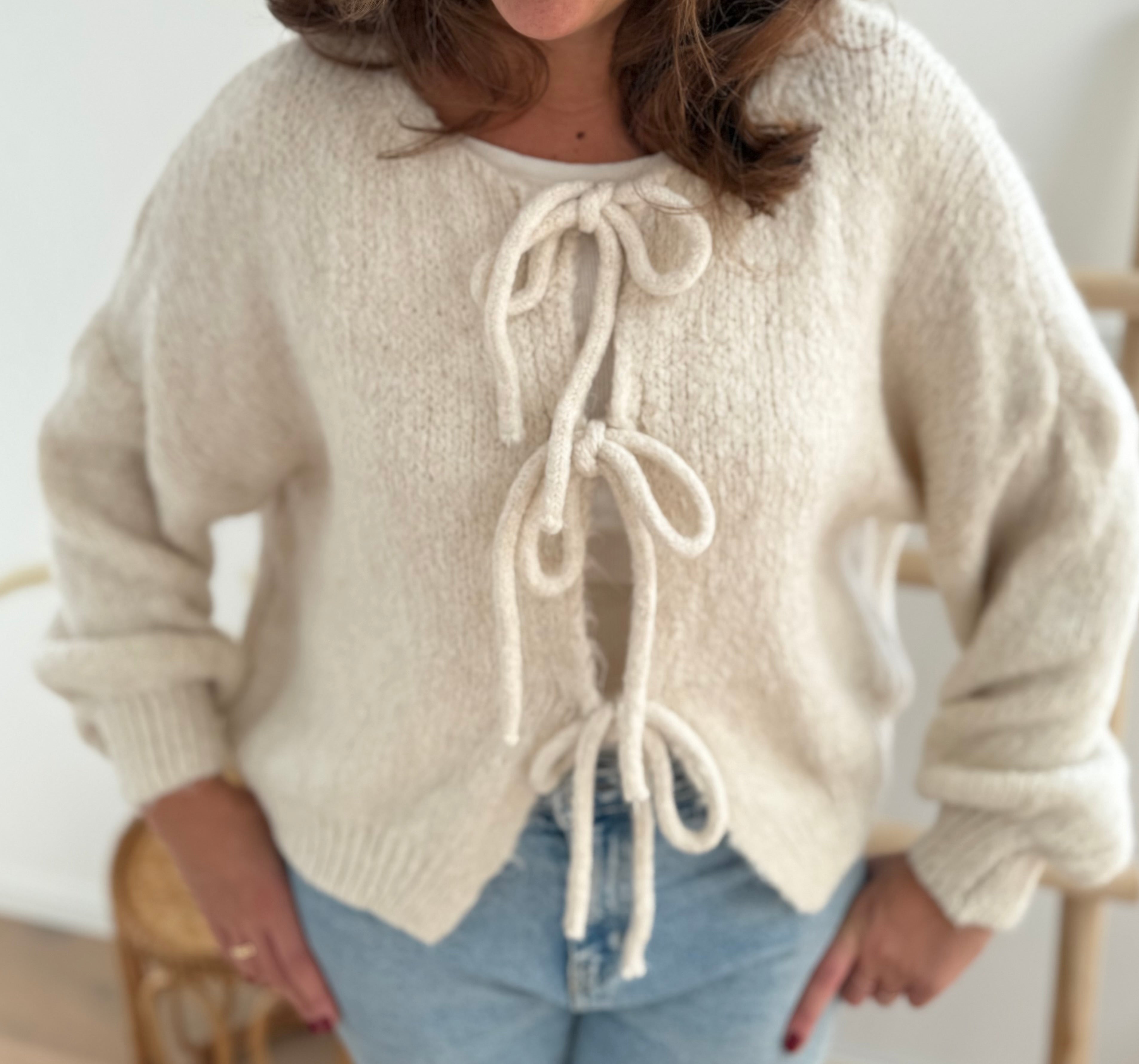 Locker fallende Strickjacke in cremeweiß die mit 3 Schleifen vorne zusammen gebunden wird.