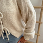 Locker fallende Strickjacke in cremeweiß die mit 3 Schleifen vorne zusammen gebunden wird.