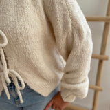 Locker fallende Strickjacke in cremeweiß die mit 3 Schleifen vorne zusammen gebunden wird.