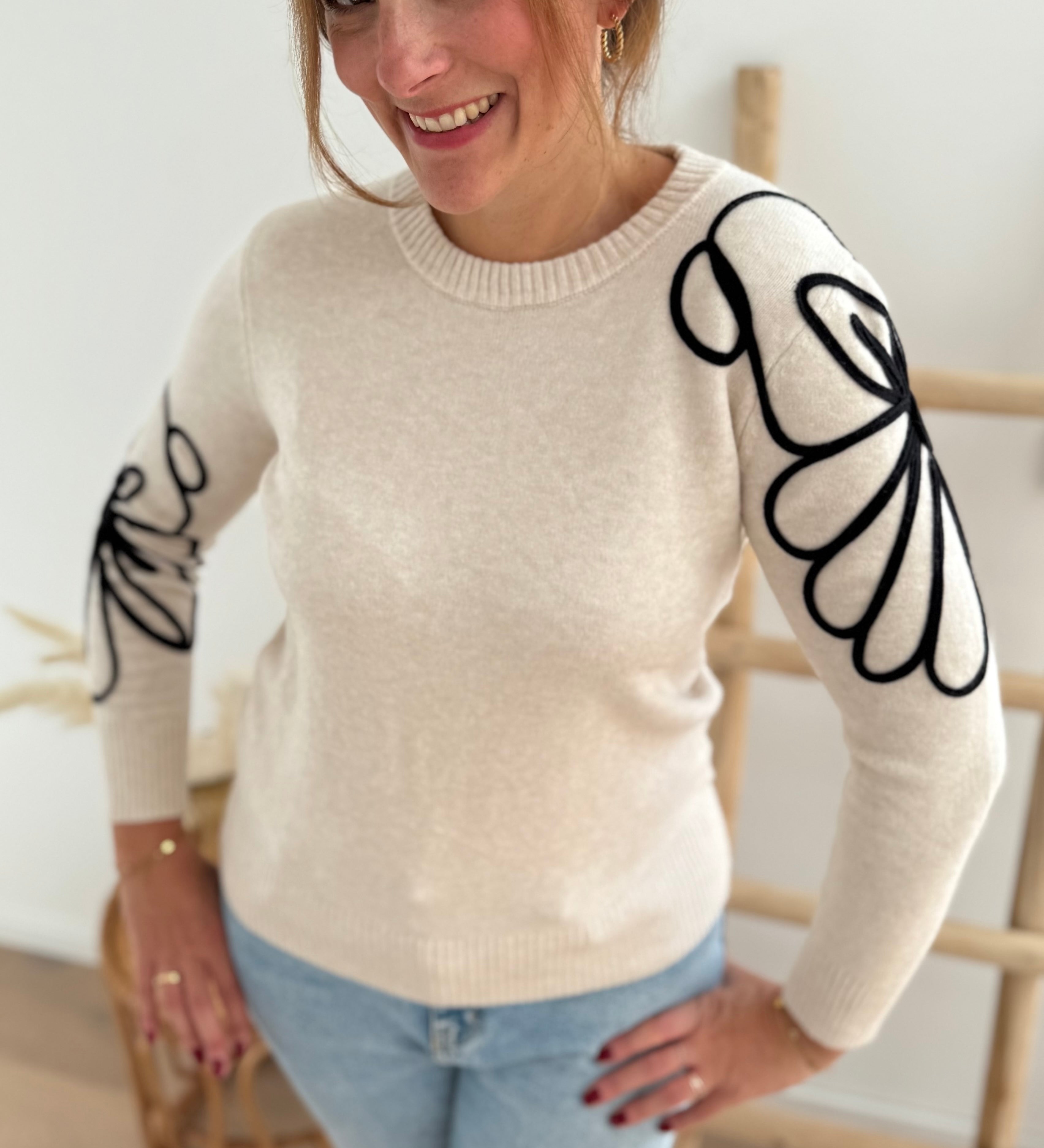 Beiger Strick Pullover mit Rundhalsausscnnitt und verspielter Blumenstickerei in schwarz an beiden Ärmeln.
