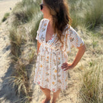 Leichtes kurzes Kleid mit V Ausschnitt und kurzen Flügelärmeln. Das Kleid ist cremefarben mit einem verspielten Blumenmuster in gelb, grün und rot.