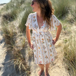 Leichtes kurzes Kleid mit V Ausschnitt und kurzen Flügelärmeln. Das Kleid ist cremefarben mit einem verspielten Blumenmuster in gelb, grün und rot.