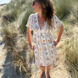 Leichtes kurzes Kleid mit V Ausschnitt und kurzen Flügelärmeln. Das Kleid ist cremefarben mit einem verspielten Blumenmuster in gelb, grün und rot.