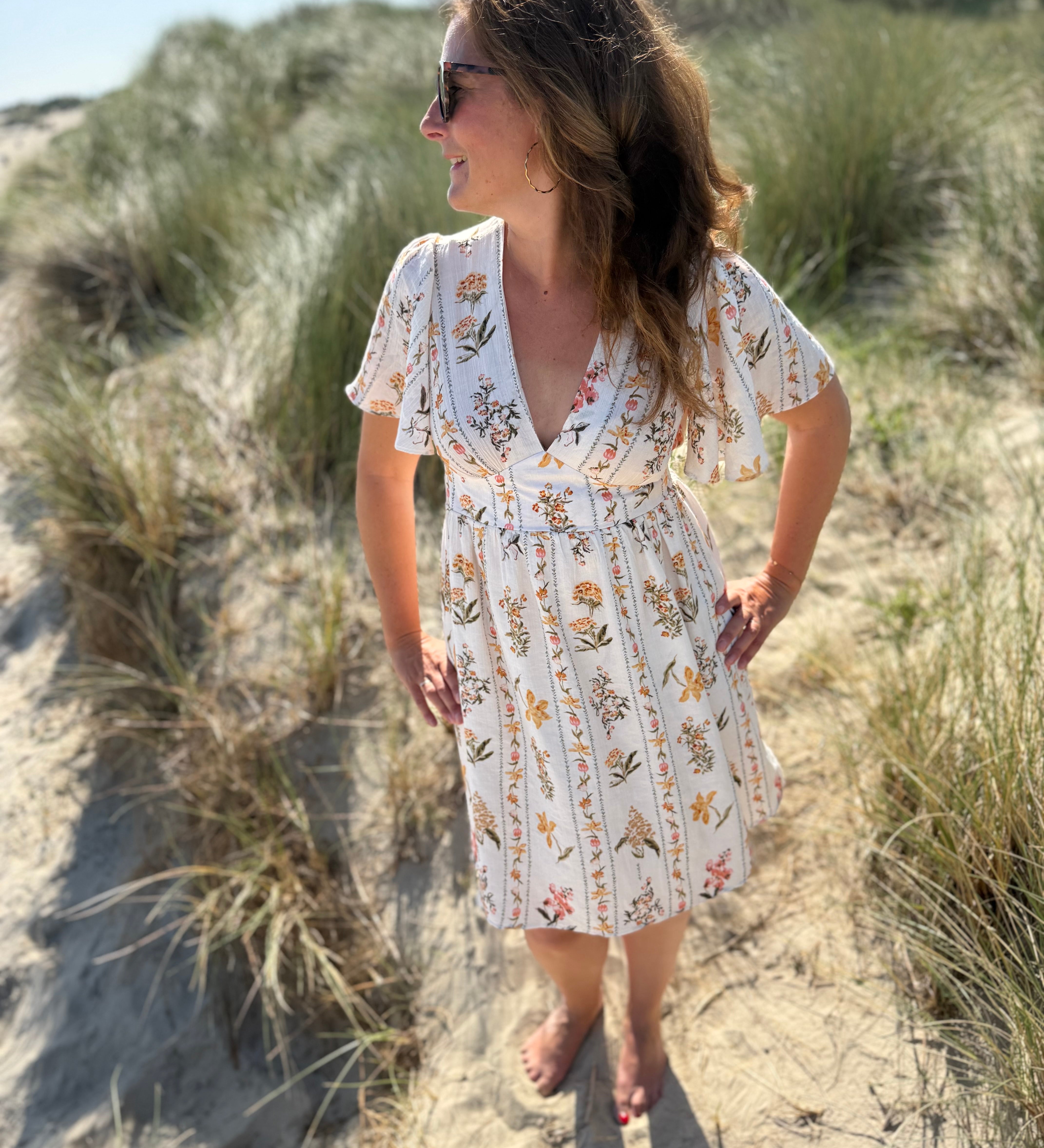Leichtes kurzes Kleid mit V Ausschnitt und kurzen Flügelärmeln. Das Kleid ist cremefarben mit einem verspielten Blumenmuster in gelb, grün und rot.
