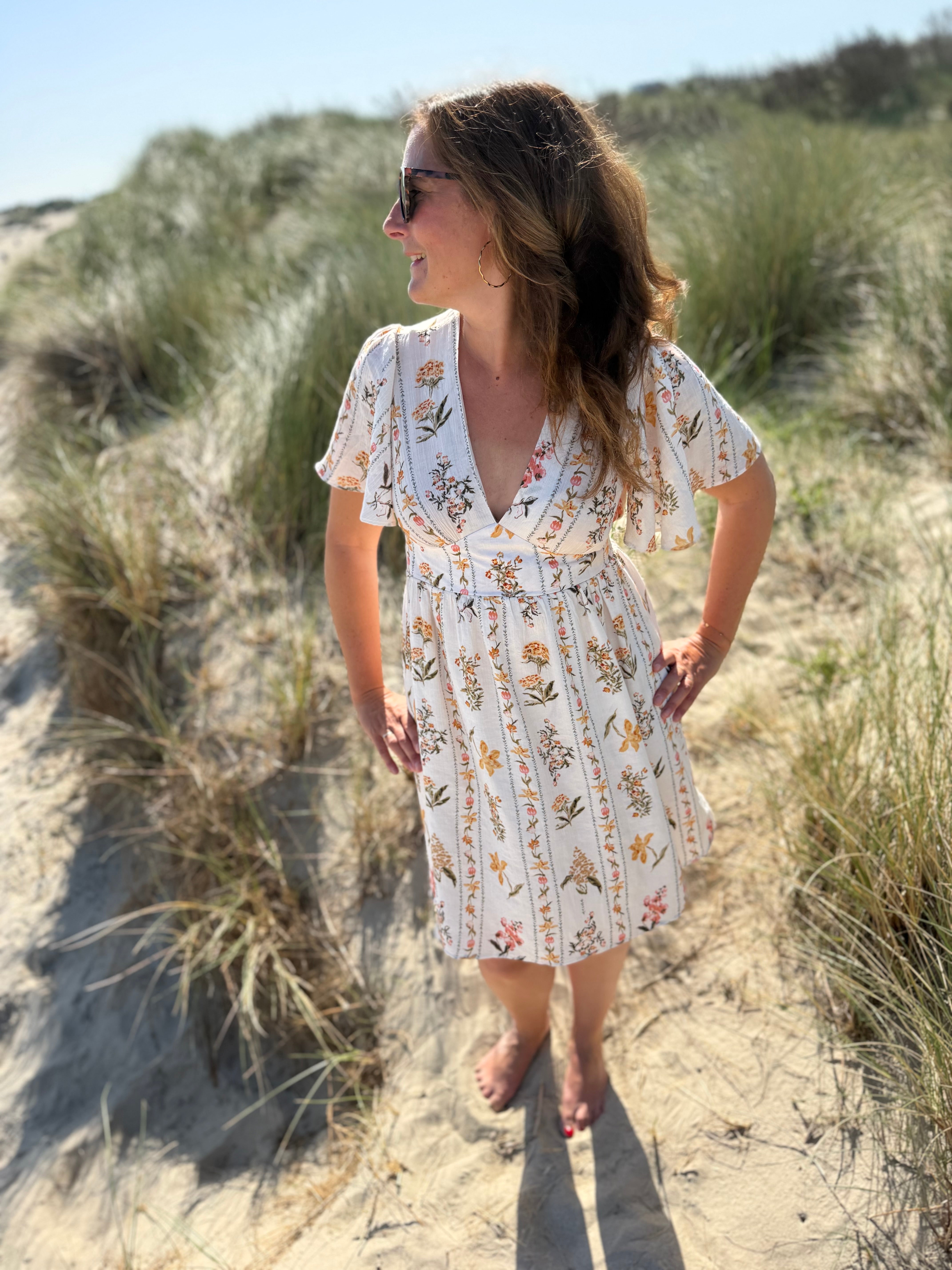 Leichtes kurzes Kleid mit V Ausschnitt und kurzen Flügelärmeln. Das Kleid ist cremefarben mit einem verspielten Blumenmuster in gelb, grün und rot.