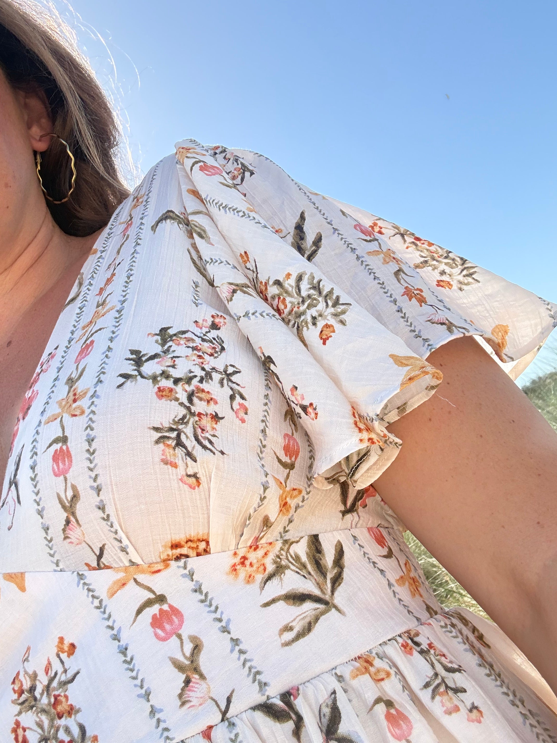 Leichtes kurzes Kleid mit V Ausschnitt und kurzen Flügelärmeln. Das Kleid ist cremefarben mit einem verspielten Blumenmuster in gelb, grün und rot.