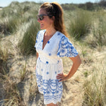Leichtes kurzes Kleid mit V Ausschnitt und kurzen Flügelärmeln. Das Kleid ist weiß mit blauen Blumenstickereien.