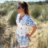 Leichtes kurzes Kleid mit V Ausschnitt und kurzen Flügelärmeln. Das Kleid ist weiß mit blauen Blumenstickereien.