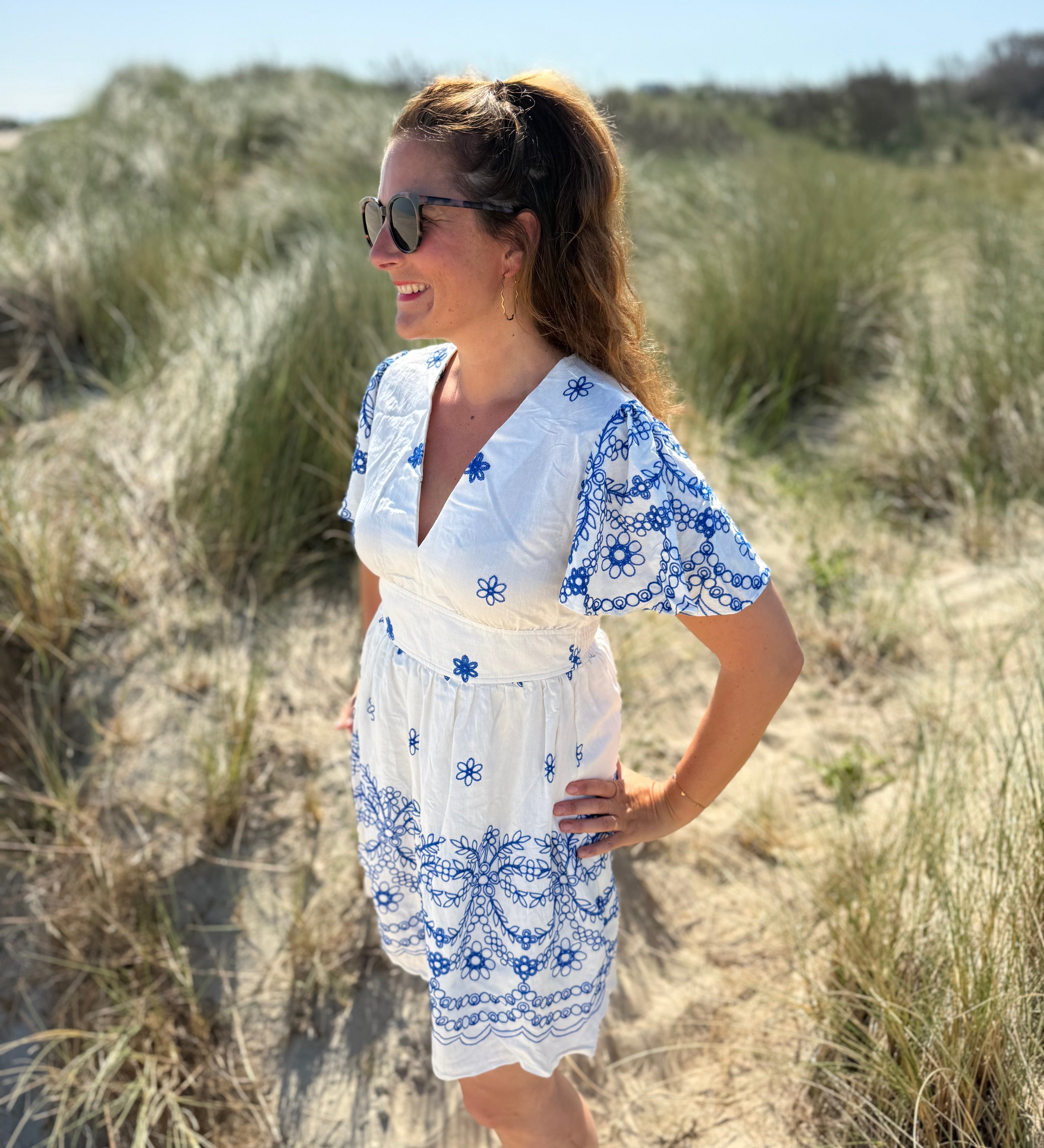 Leichtes kurzes Kleid mit V Ausschnitt und kurzen Flügelärmeln. Das Kleid ist weiß mit blauen Blumenstickereien.