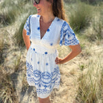 Leichtes kurzes Kleid mit V Ausschnitt und kurzen Flügelärmeln. Das Kleid ist weiß mit blauen Blumenstickereien.
