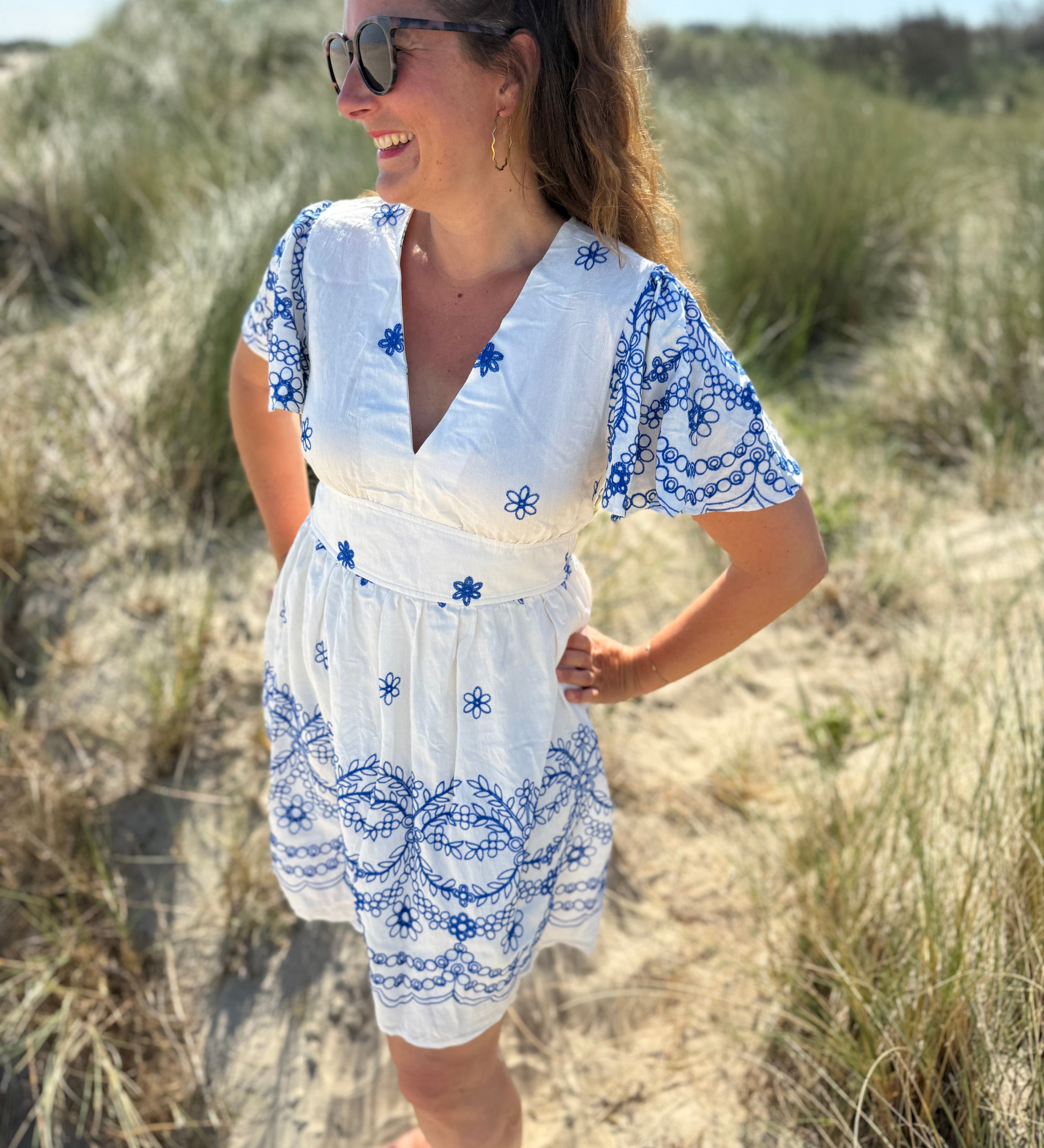 Leichtes kurzes Kleid mit V Ausschnitt und kurzen Flügelärmeln. Das Kleid ist weiß mit blauen Blumenstickereien.