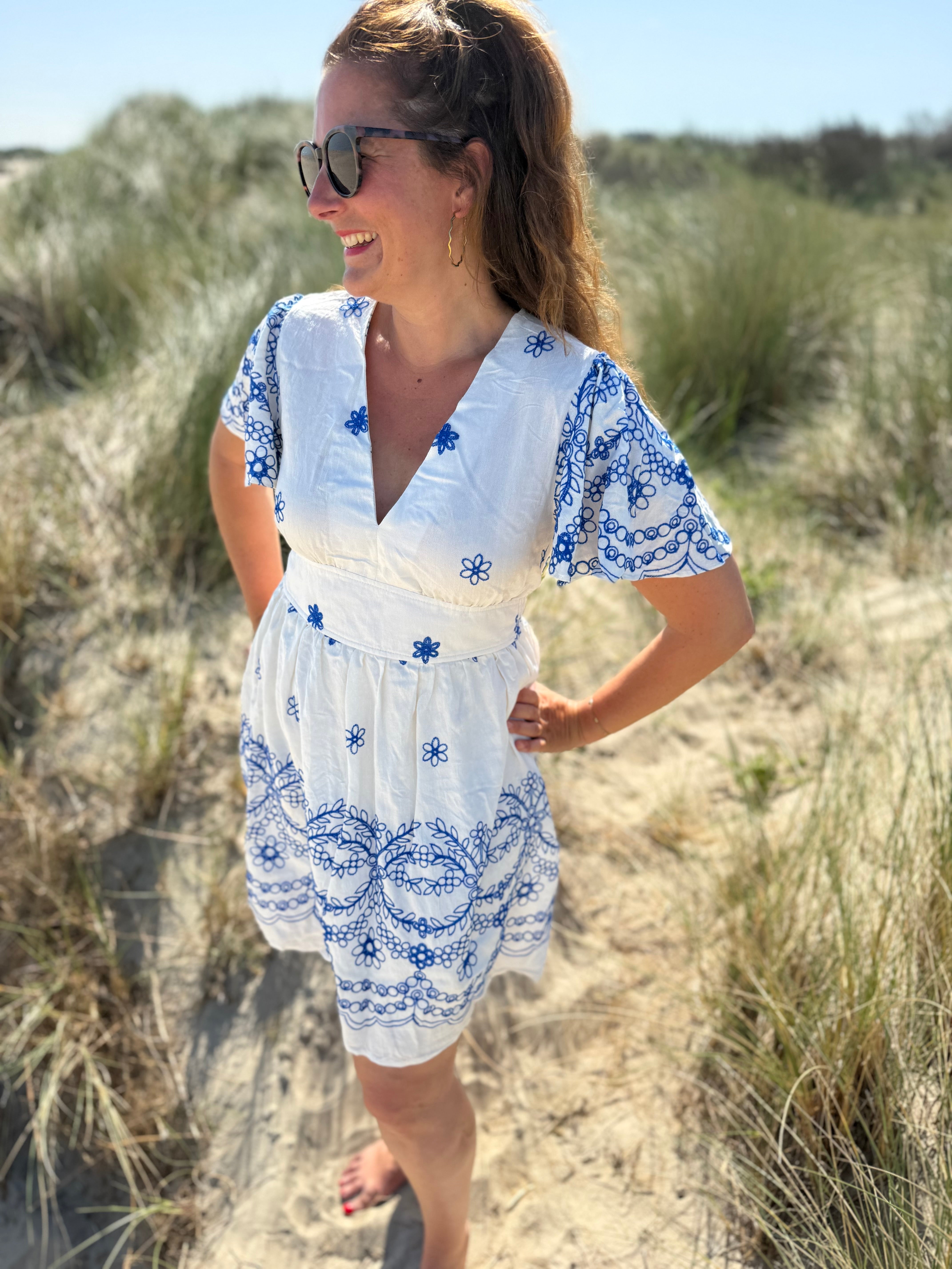 Leichtes kurzes Kleid mit V Ausschnitt und kurzen Flügelärmeln. Das Kleid ist weiß mit blauen Blumenstickereien.